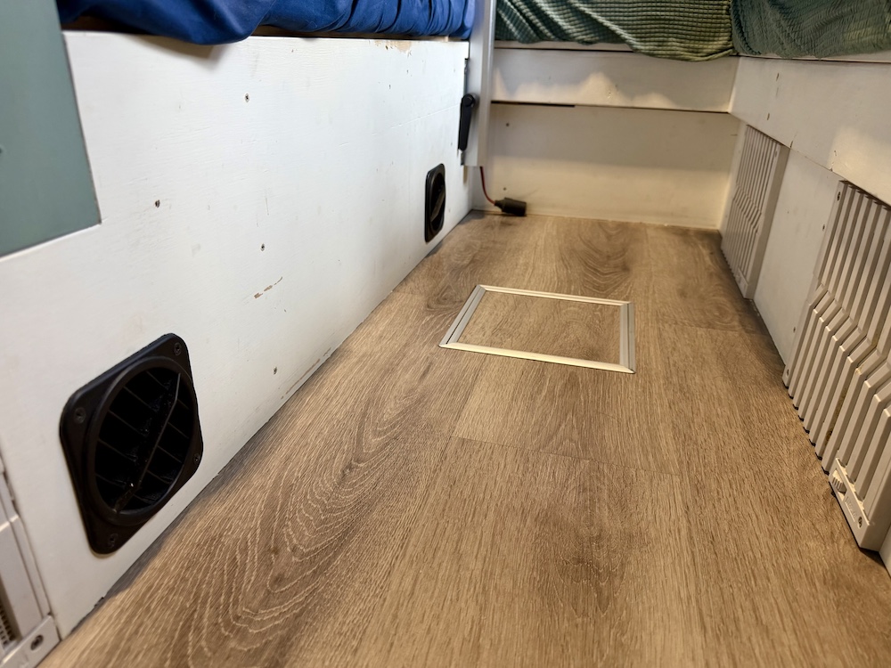 キャンピングカーの居住空間の足元に設置したFFヒーターの黒い温風吹出口